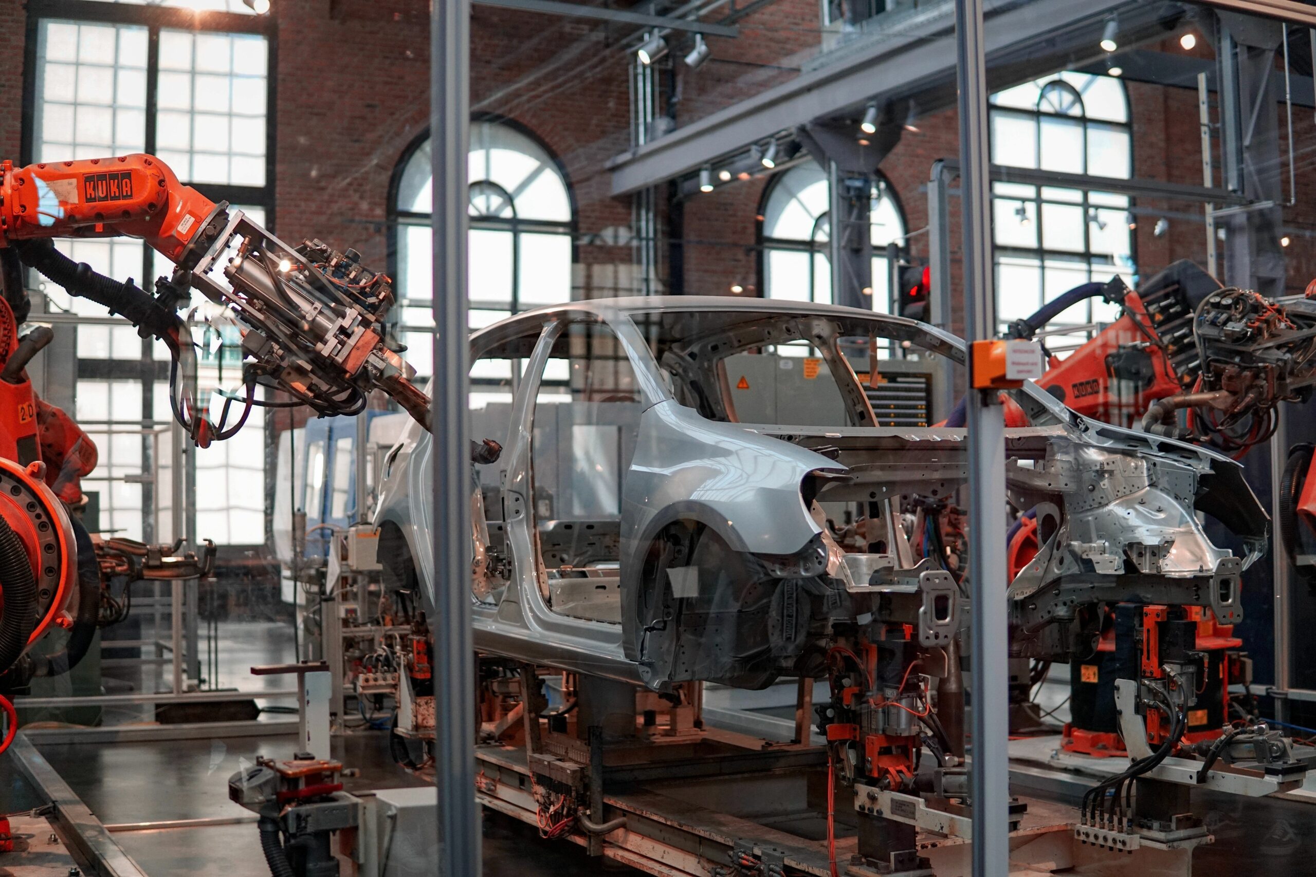 Dekoratives Symbolfoto zeigt Roboterarme in einer Autofabrik bei der Arbeit an einer silbernen Karosserie.